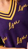 A woman modeling a purple knit sweater with yellow and white striped trim and 'LSU' script lettering, paired with blue jeans against a plain white background.