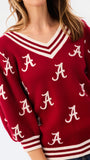 A woman wearing a crimson red V-neck sweater with white stripes and white Alabama 'A' logos, paired with blue jeans, against a plain white background.