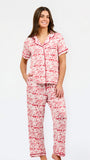 A woman modeling a two-piece pajama set with a red and white toile-style print, featuring a short-sleeve button-front top with a red tie collar and matching drawstring pants, against a plain white studio background.