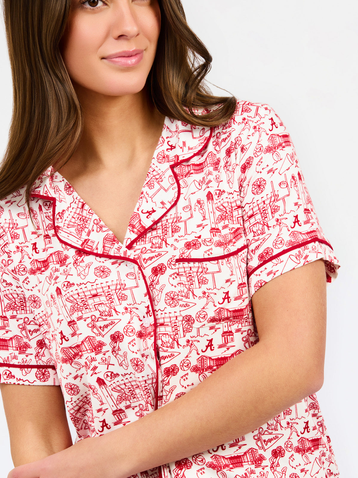 A woman modeling a two-piece pajama set with a red and white toile-style print, featuring a short-sleeve button-front top with a red tie collar and matching drawstring pants, against a plain white studio background.