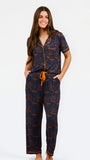 A woman modeling a short-sleeve pajama set with an orange and navy blue patterned design, featuring a collared top with a front zipper and drawstring, and matching pants.