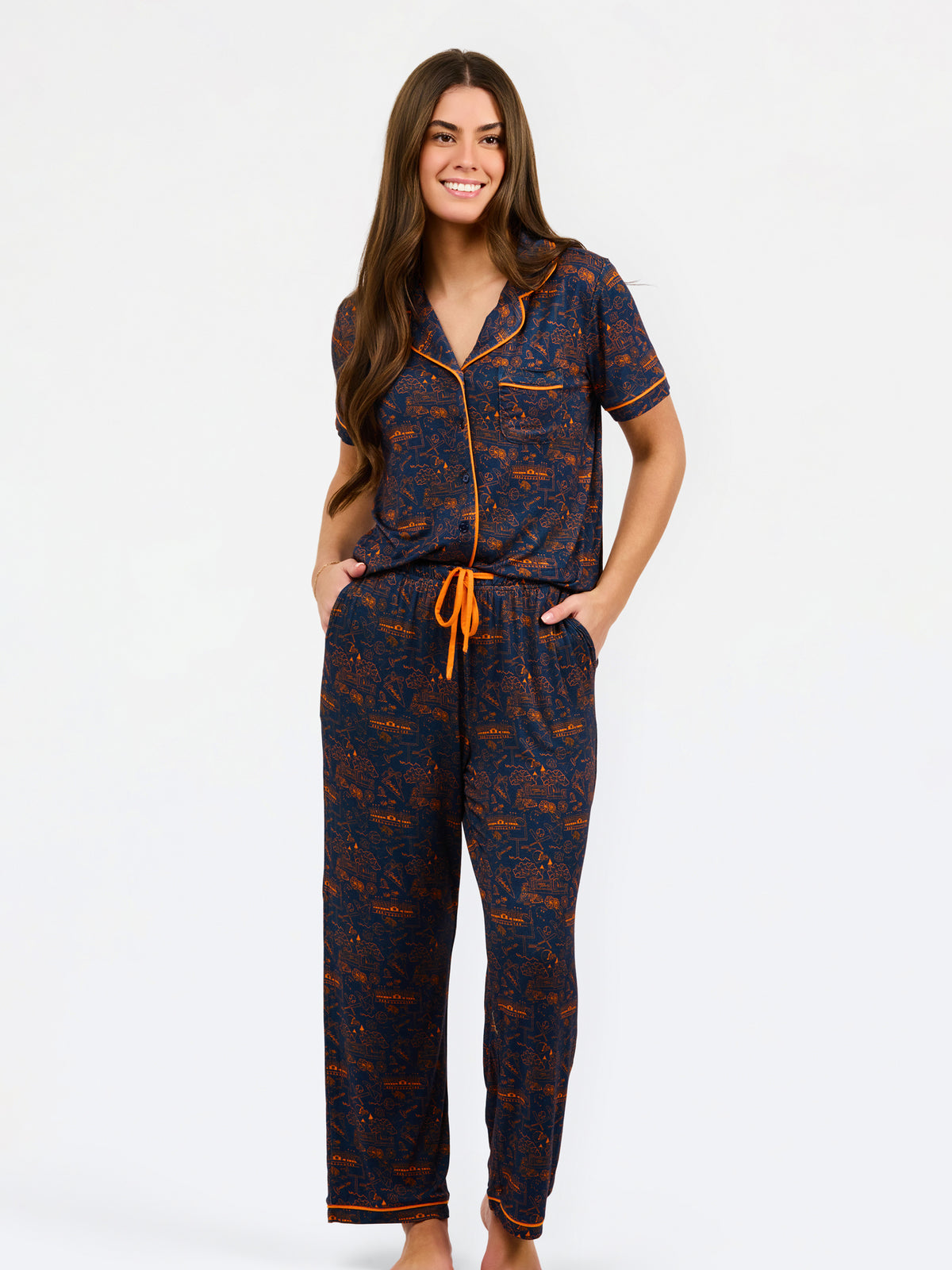 A woman modeling a short-sleeve pajama set with an orange and navy blue patterned design, featuring a collared top with a front zipper and drawstring, and matching pants.