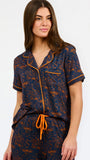 A woman modeling a short-sleeve pajama set with an orange and navy blue patterned design, featuring a collared top with a front zipper and drawstring, and matching pants.