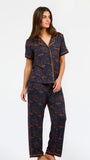 A woman modeling a short-sleeve pajama set with an orange and navy blue patterned design, featuring a collared top with a front zipper and drawstring, and matching pants.