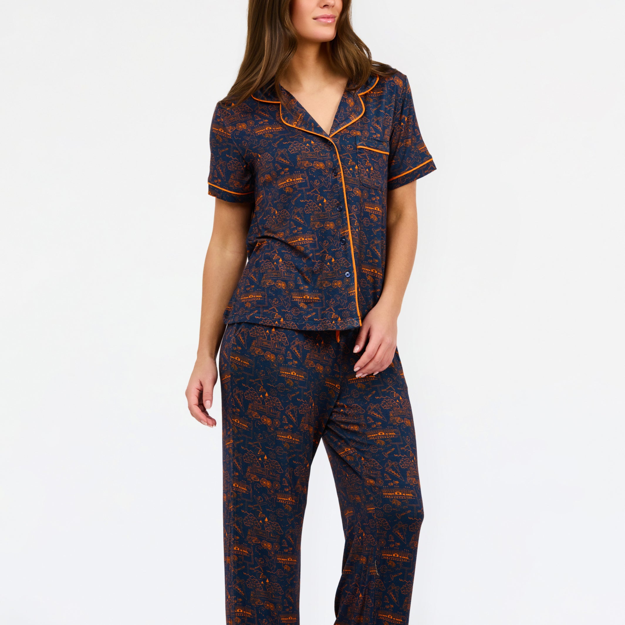 A woman modeling a short-sleeve pajama set with an orange and navy blue patterned design, featuring a collared top with a front zipper and drawstring, and matching pants.