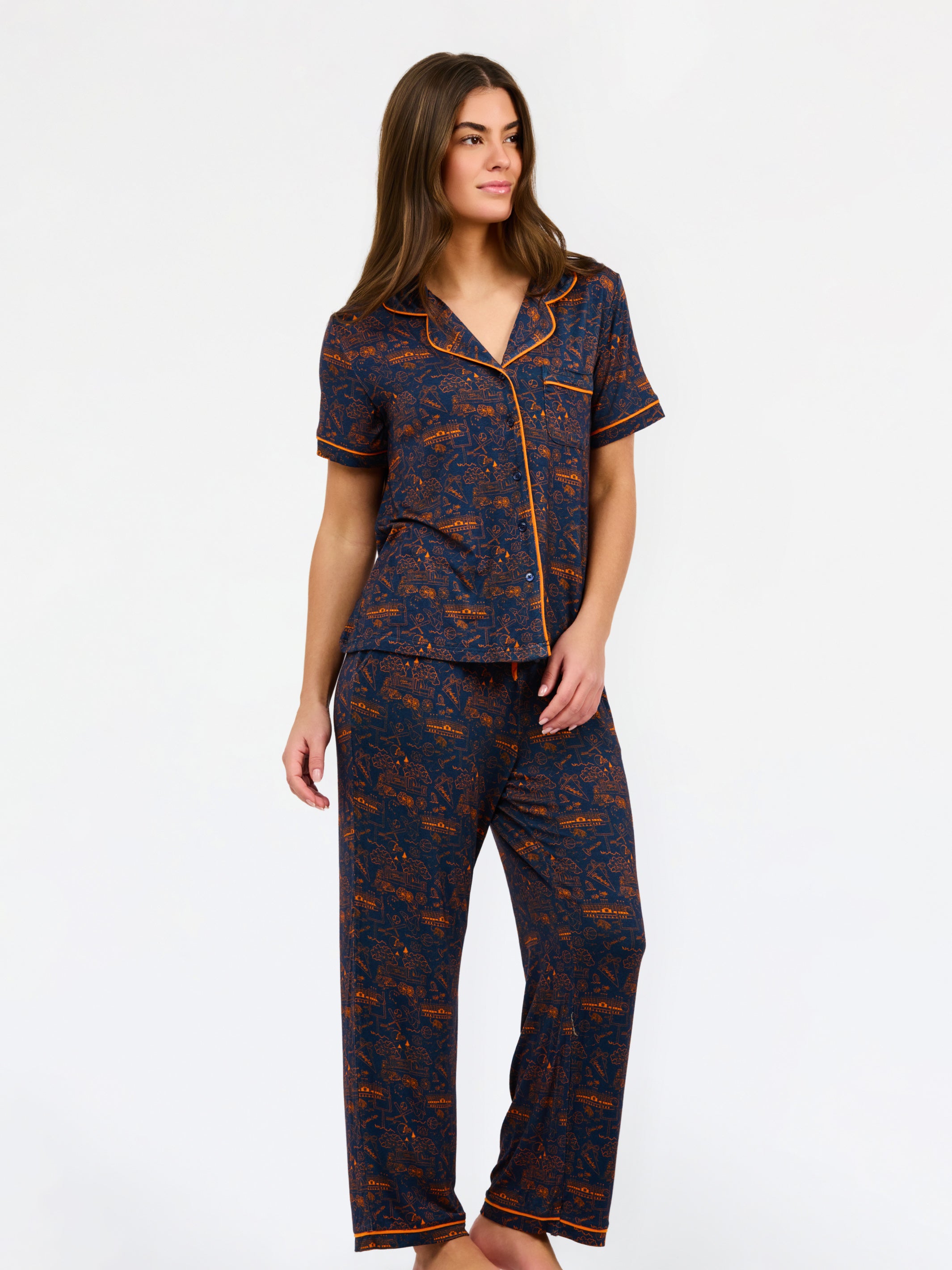A woman modeling a short-sleeve pajama set with an orange and navy blue patterned design, featuring a collared top with a front zipper and drawstring, and matching pants.