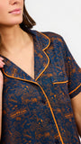 A woman modeling a short-sleeve pajama set with an orange and navy blue patterned design, featuring a collared top with a front zipper and drawstring, and matching pants.
