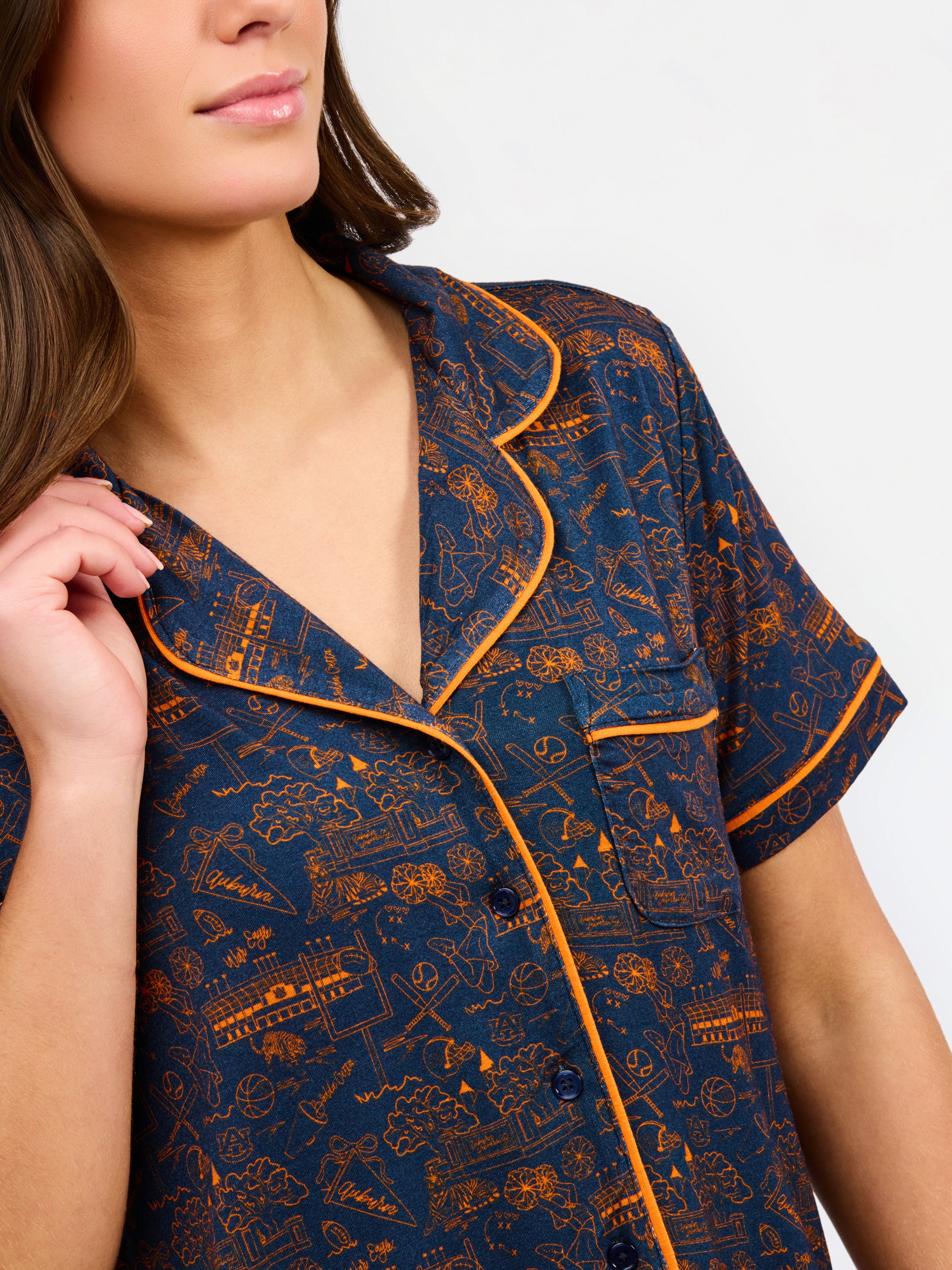 A woman modeling a short-sleeve pajama set with an orange and navy blue patterned design, featuring a collared top with a front zipper and drawstring, and matching pants.