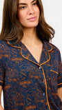 A woman modeling a short-sleeve pajama set with an orange and navy blue patterned design, featuring a collared top with a front zipper and drawstring, and matching pants.
