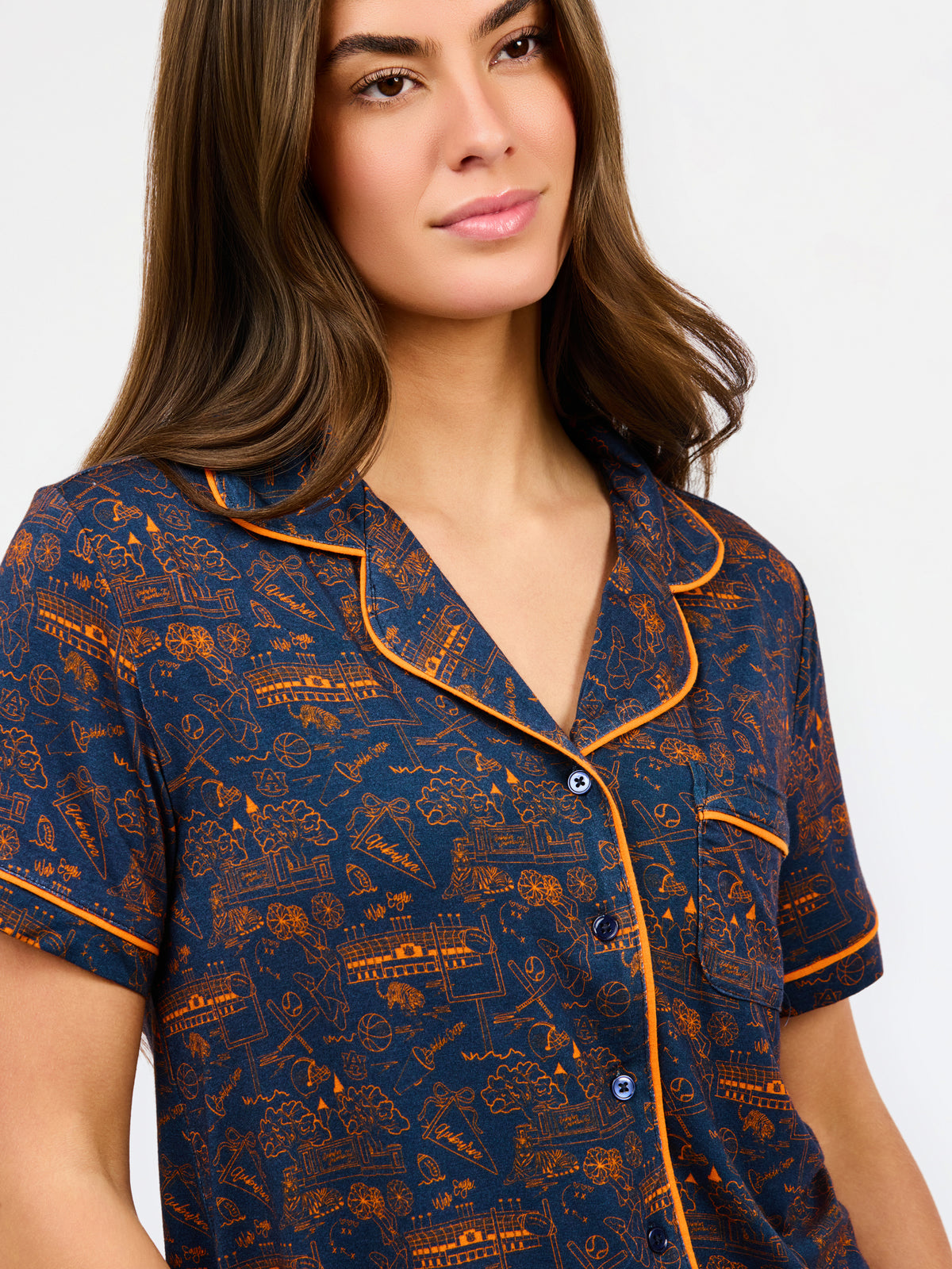 A woman modeling a short-sleeve pajama set with an orange and navy blue patterned design, featuring a collared top with a front zipper and drawstring, and matching pants.