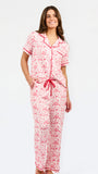 A woman modeling a two-piece pajama set featuring a short-sleeve button-front top and matching pants, red toile print with red piping and a red drawstring waist.
