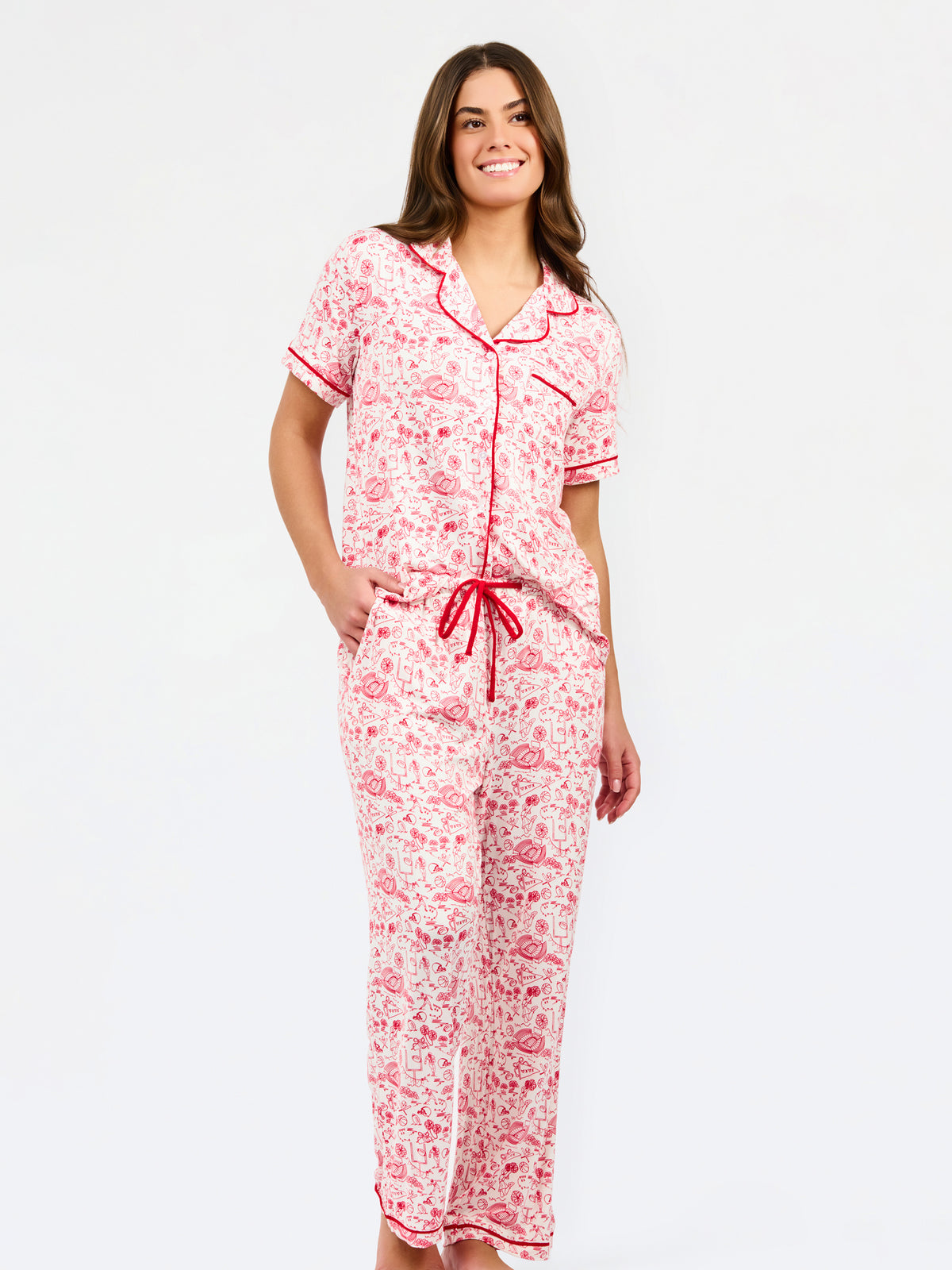 A woman modeling a two-piece pajama set featuring a short-sleeve button-front top and matching pants, red toile print with red piping and a red drawstring waist.