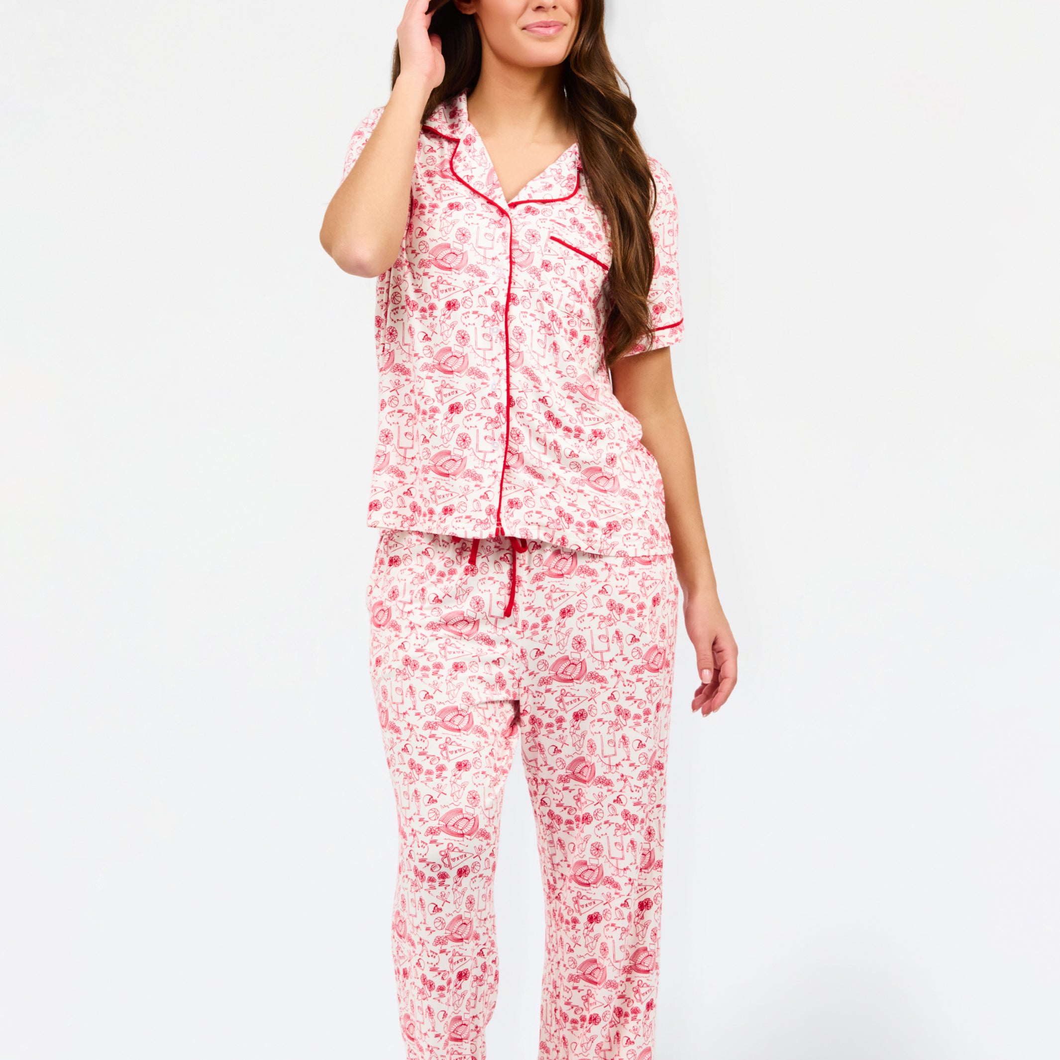 A woman modeling a two-piece pajama set featuring a short-sleeve button-front top and matching pants, red toile print with red piping and a red drawstring waist.