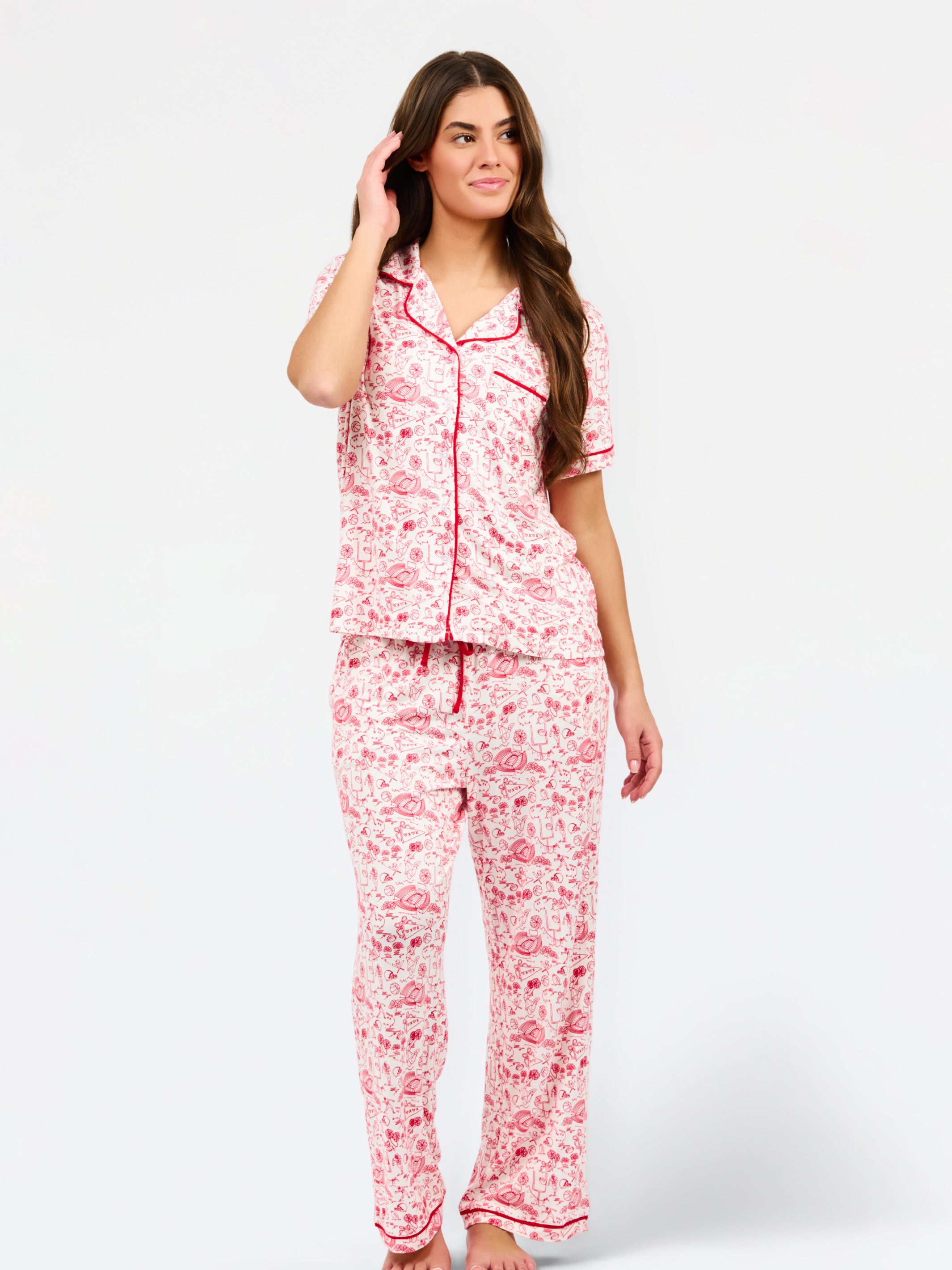 A woman modeling a two-piece pajama set featuring a short-sleeve button-front top and matching pants, red toile print with red piping and a red drawstring waist.