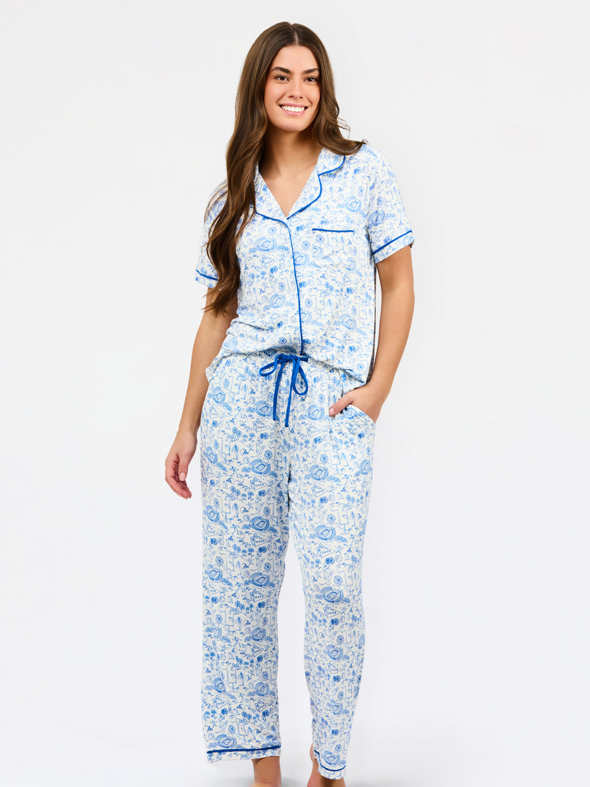 A woman modeling a two-piece pajama set with a light blue and white football toile, featuring a short-sleeve button-front top and matching pants with a drawstring waist.
