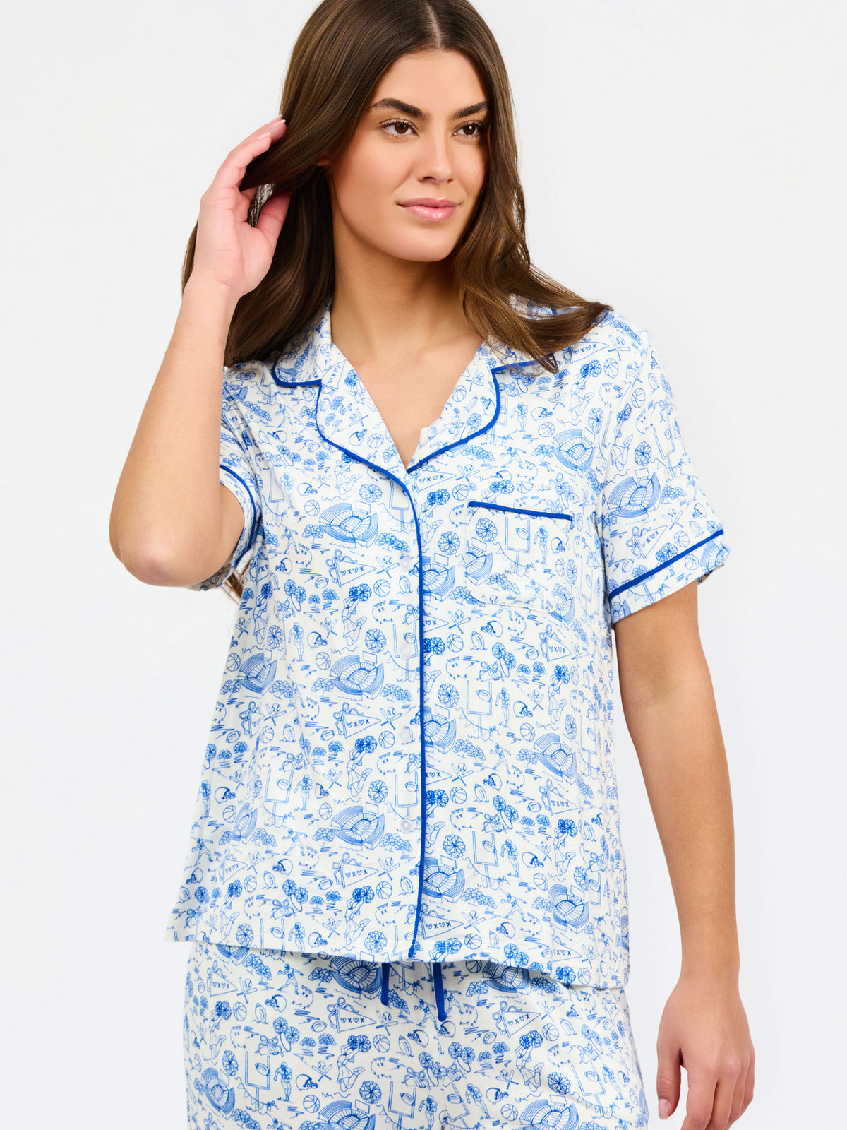 A woman modeling a matching short-sleeve pajama set with a blue and white toile pattern and blue piping, against a plain white studio background.