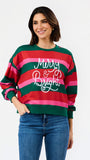 A woman wearing a festive holiday striped sweater with green, red, and pink horizontal stripes and 'Merry & Bright' written in white script across the chest, paired with blue jeans against a plain white background.