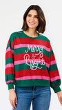 A woman wearing a festive crewneck sweatshirt with horizontal red, green, and pink stripes, featuring the text 'Merry & Bright' in white script across the chest. She is paired with blue jeans against a clean white background.