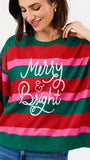 A woman wearing a festive holiday striped sweatshirt with green, red, and pink horizontal stripes and 'Merry & Bright' written in white script across the front.