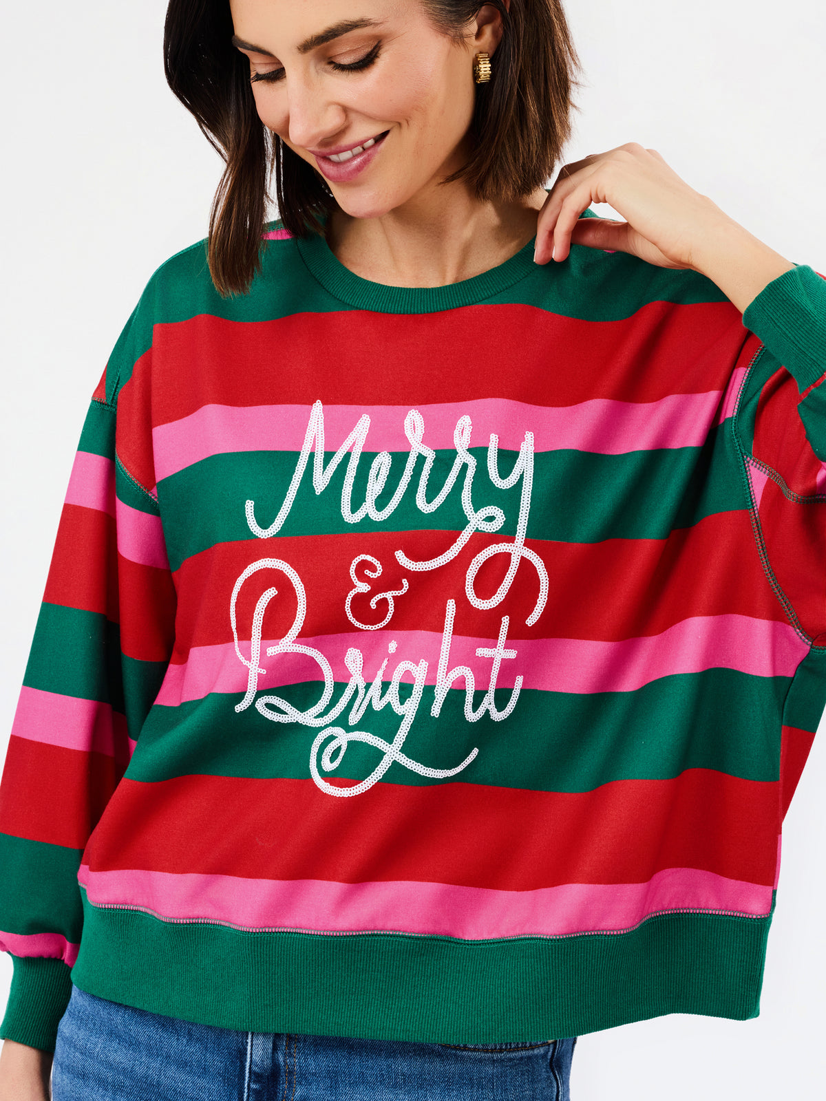 A woman wearing a festive holiday striped sweatshirt with green, red, and pink horizontal stripes and 'Merry & Bright' written in white script across the front.