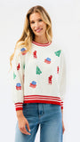 A woman wearing a cream-colored Christmas crewneck sweater with red and white striped trim and green/red holiday motifs, paired with blue jeans, against a plain white background.
