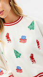 A close-up of a woman wearing a white crewneck sweatshirt with red striped trim and a festive Christmas print featuring Santa Claus, Christmas trees, and gift boxes.