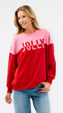 A woman wearing a color-blocked crewneck sweatshirt with a pink upper section and red lower section, featuring the word 'JOLLY' printed in white across the chest, paired with blue jeans against a plain white background.
