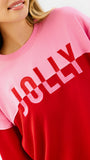 A woman wearing a color-blocked crewneck sweatshirt with a pink upper section and red lower section, featuring the word 'JOLLY' printed in white across the chest, paired with blue jeans against a plain white background.