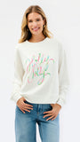 A woman wearing a cream-colored crewneck sweatshirt with 'Holly Jolly' written in a colorful pastel script across the chest, paired with blue jeans, against a plain white background.