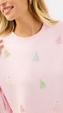 A close-up of a woman wearing a light pink crewneck sweatshirt decorated with small, colorful sequined Christmas tree motifs.