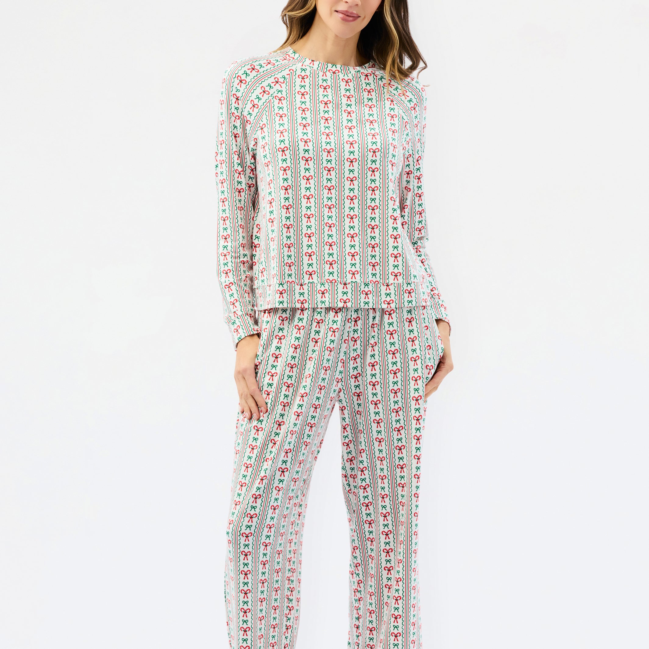 A woman modeling a matching two-piece pajama set with a long-sleeve top and wide-leg pants, featuring a vertical multicolor pattern of small illustrated figures on a light background, set against a plain white studio background.