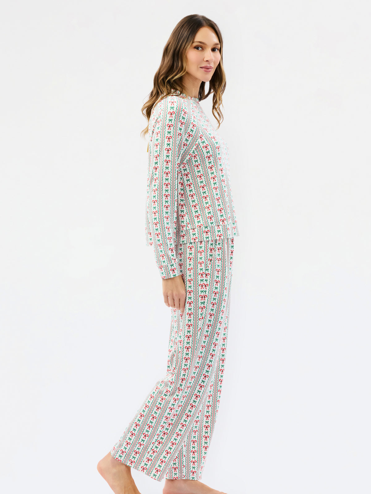 A woman modeling a matching two-piece pajama set with a white base and vertical red and green striped pattern, shown from a side profile against a plain white studio background.