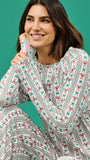 A woman wearing a long-sleeve white tunic with a red and green bow and stripe pattern, posed against a solid teal background.