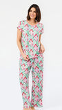 A woman modeling a matching short-sleeve pajama set with an all-over geometric pattern in mint green, pink, and red on a white background, photographed against a clean white studio backdrop.