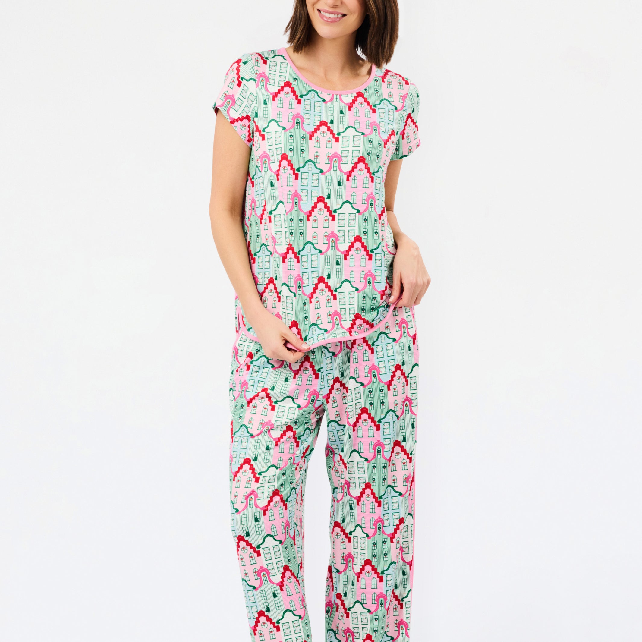 A woman modeling a matching short-sleeve pajama set with an all-over geometric pattern in mint green, pink, and red on a white background, photographed against a clean white studio backdrop.