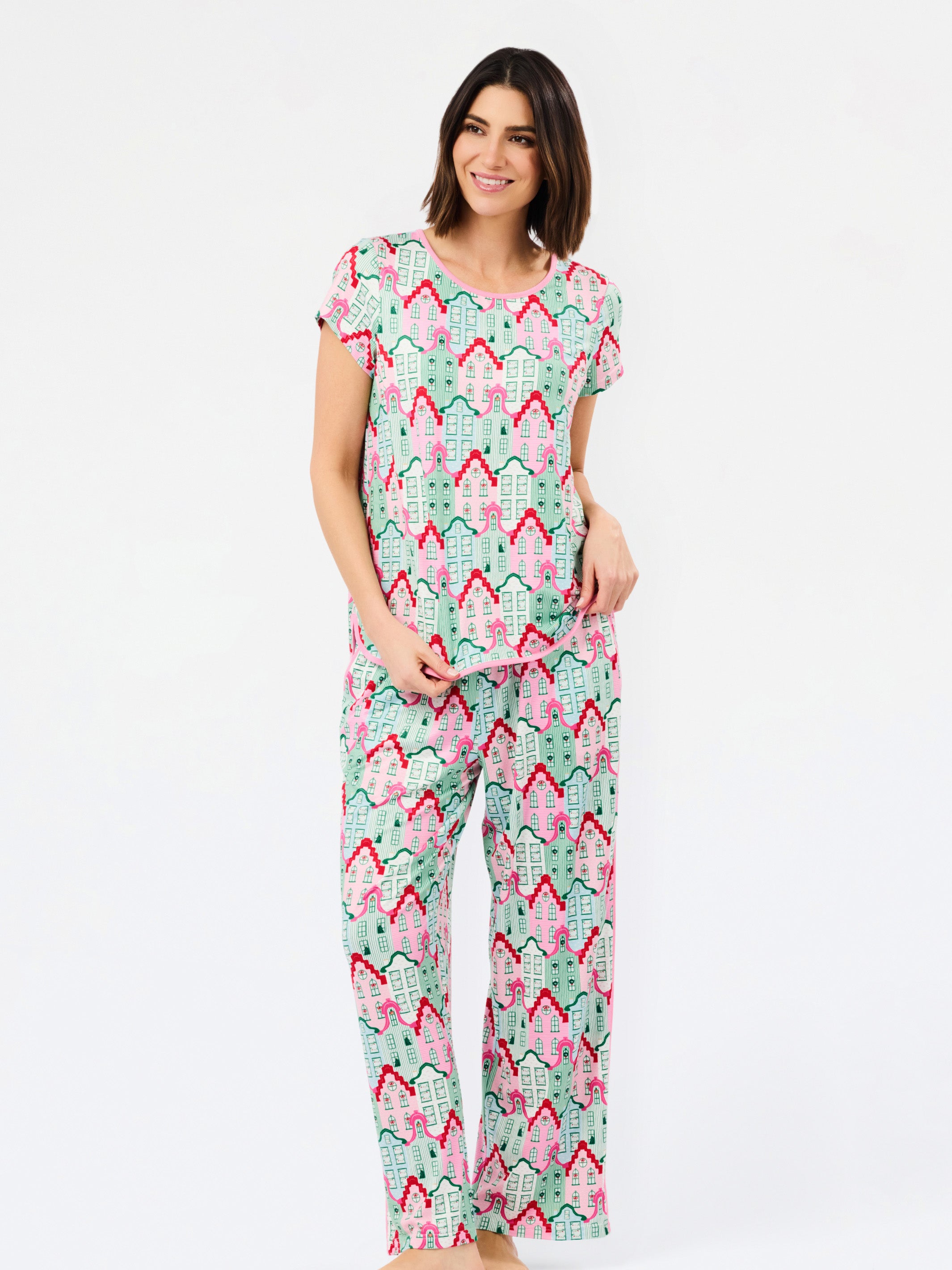 A woman modeling a matching short-sleeve pajama set with an all-over geometric pattern in mint green, pink, and red on a white background, photographed against a clean white studio backdrop.