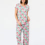 A woman modeling a matching short-sleeve pajama set with an all-over geometric pattern in mint green, pink, and red on a white background, photographed against a clean white studio backdrop.