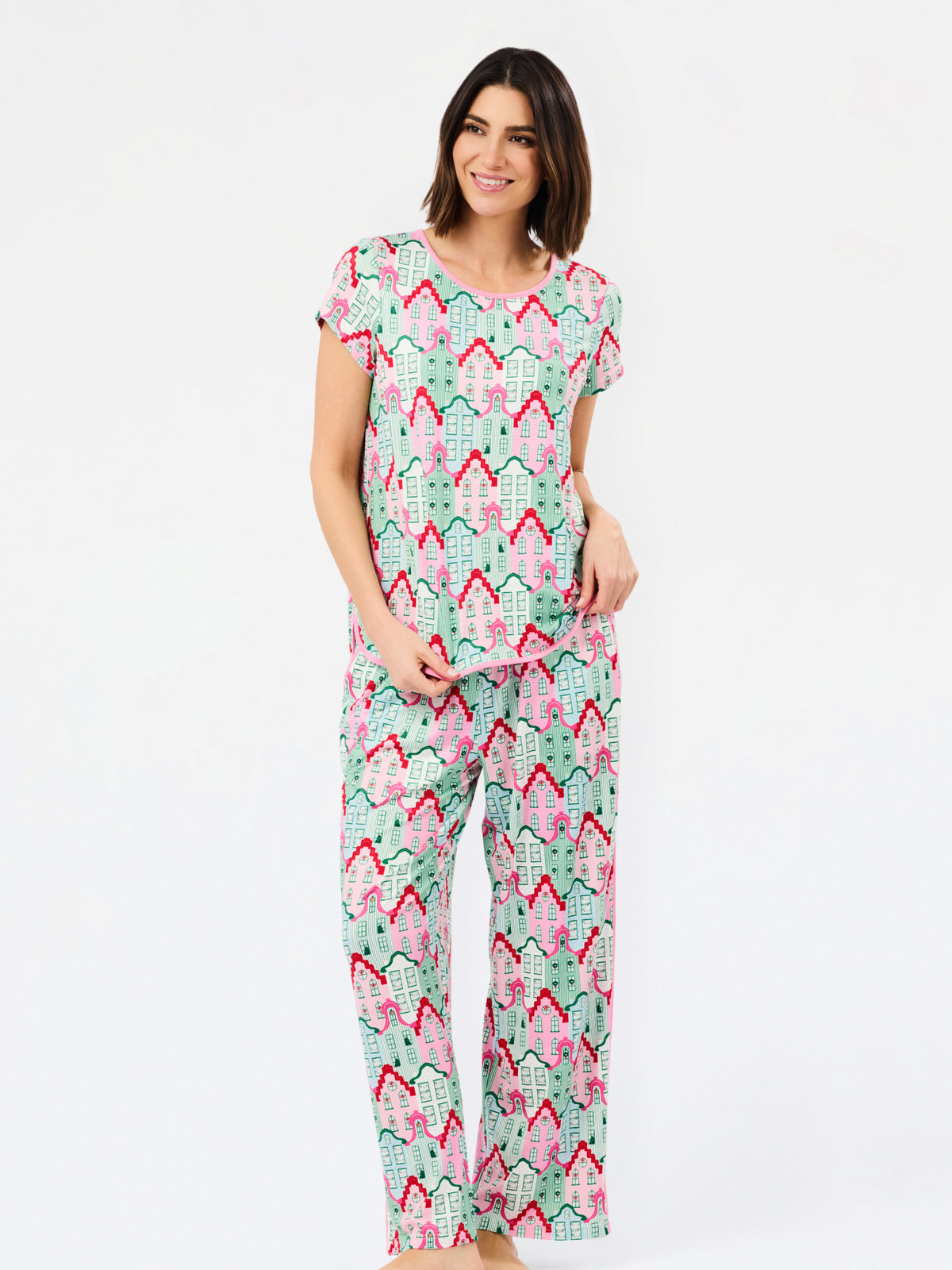 A woman modeling a matching short-sleeve pajama set with an all-over geometric pattern in mint green, pink, and red on a white background, photographed against a clean white studio backdrop.