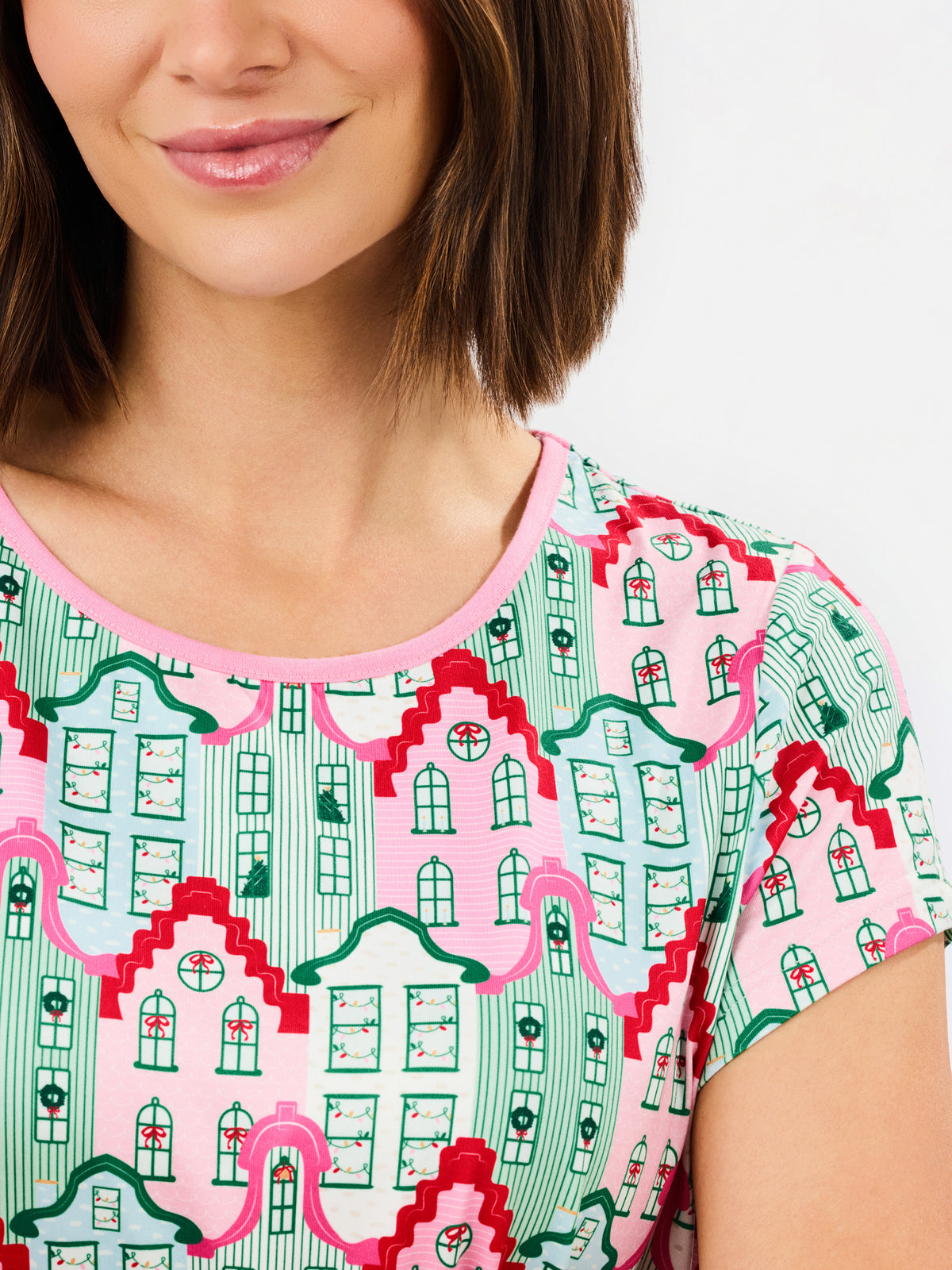 A close-up of a woman wearing a short-sleeve top with a colorful architectural house pattern in pink, green, and red on a light background.