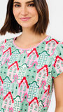 A woman wearing a short-sleeve crewneck top with a colorful repeating pattern of stylized houses in pink, green, and red on a light background.