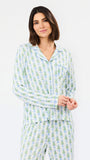 A woman modeling a matching long-sleeve pajama set with a light blue and green pine tree pattern on a white background, photographed against a clean white studio backdrop.