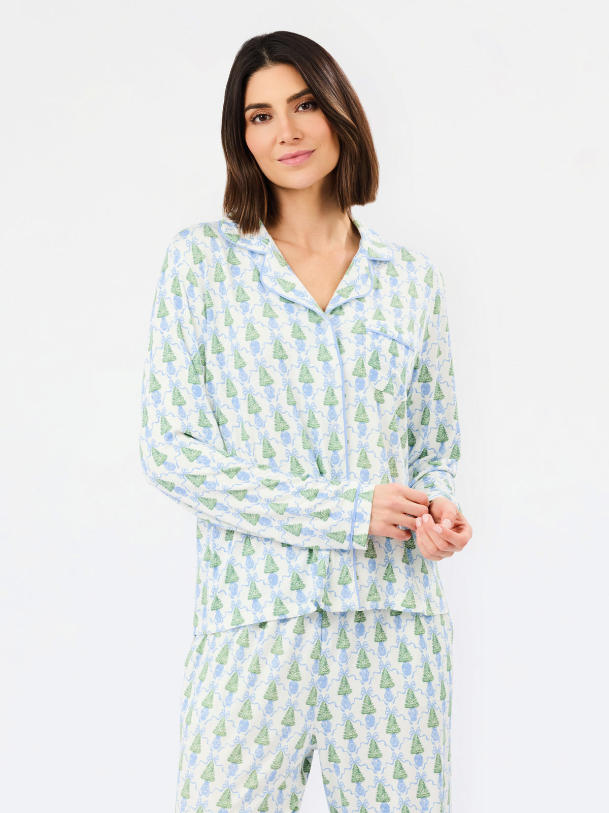 A woman modeling a matching long-sleeve pajama set with a light blue and green pine tree pattern on a white background, photographed against a clean white studio backdrop.