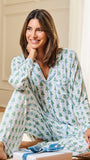 A woman wearing a light blue and white pajama set with a green pine tree pattern, sitting on a floor in a bright room with wrapped gifts in the foreground.