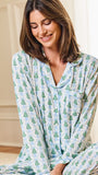 A woman wearing a light blue and white long-sleeve pajama set with a green pine tree pattern, sitting in a brightly lit room.