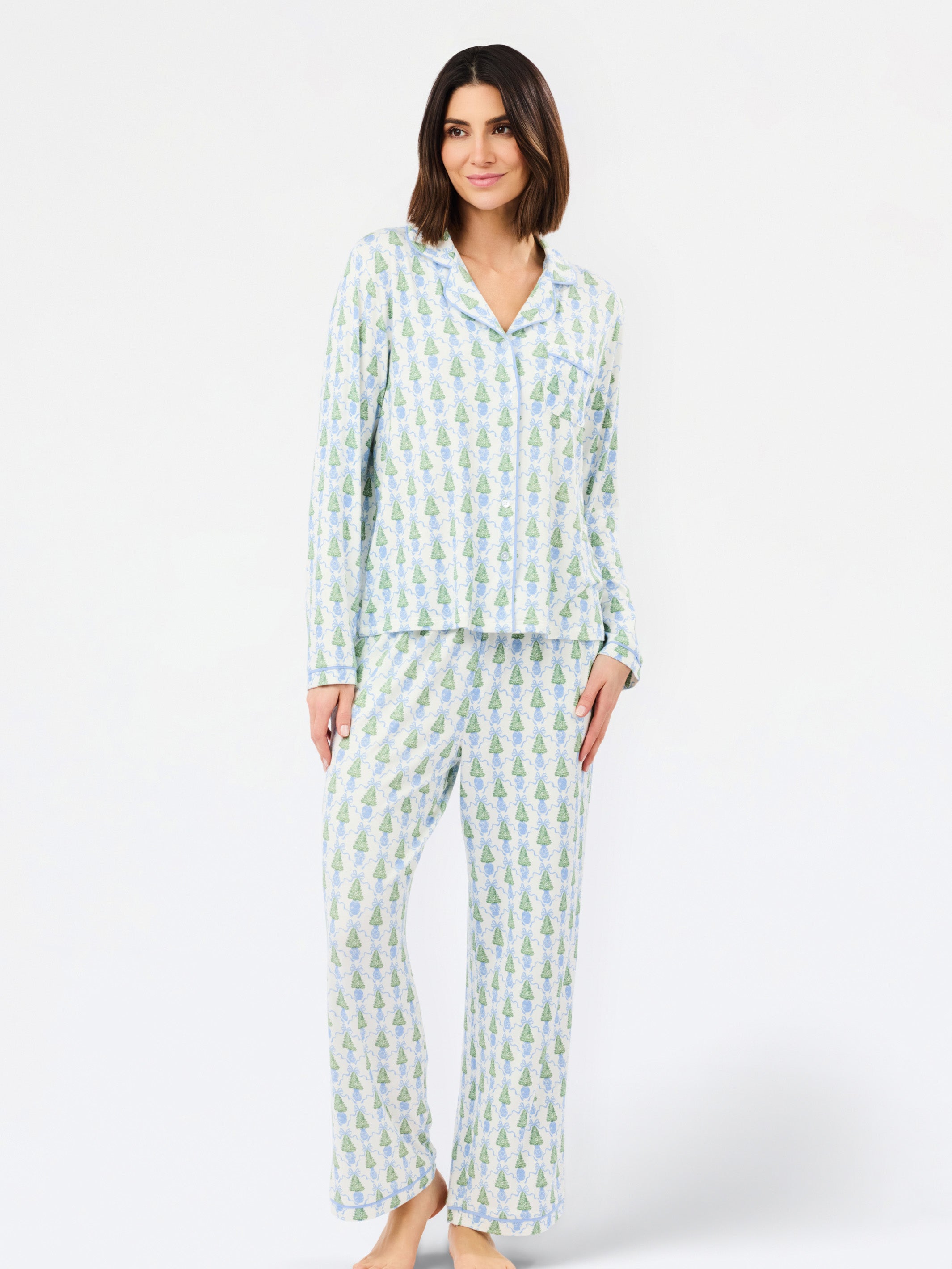 A woman modeling a two-piece long-sleeve pajama set with a light blue and white pineapple print, standing against a plain white studio background.