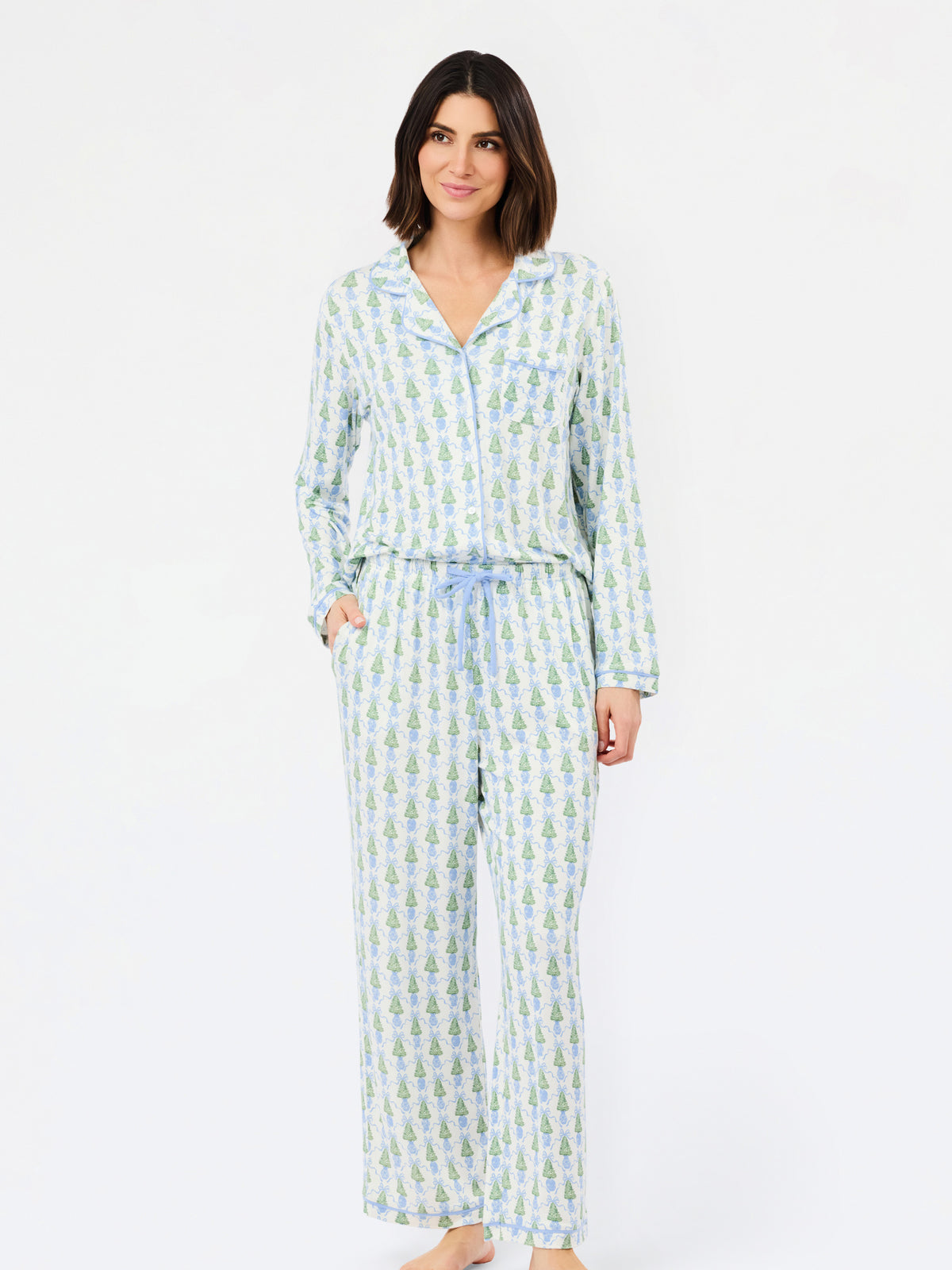 A woman modeling a matching long-sleeve pajama set with a light blue and green pineapple print, featuring a button-up top and matching pants with a drawstring waist, against a plain white background.