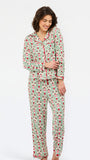 A woman modeling a two-piece pajama set with a green and pink floral print and red piping, standing against a plain white studio background.