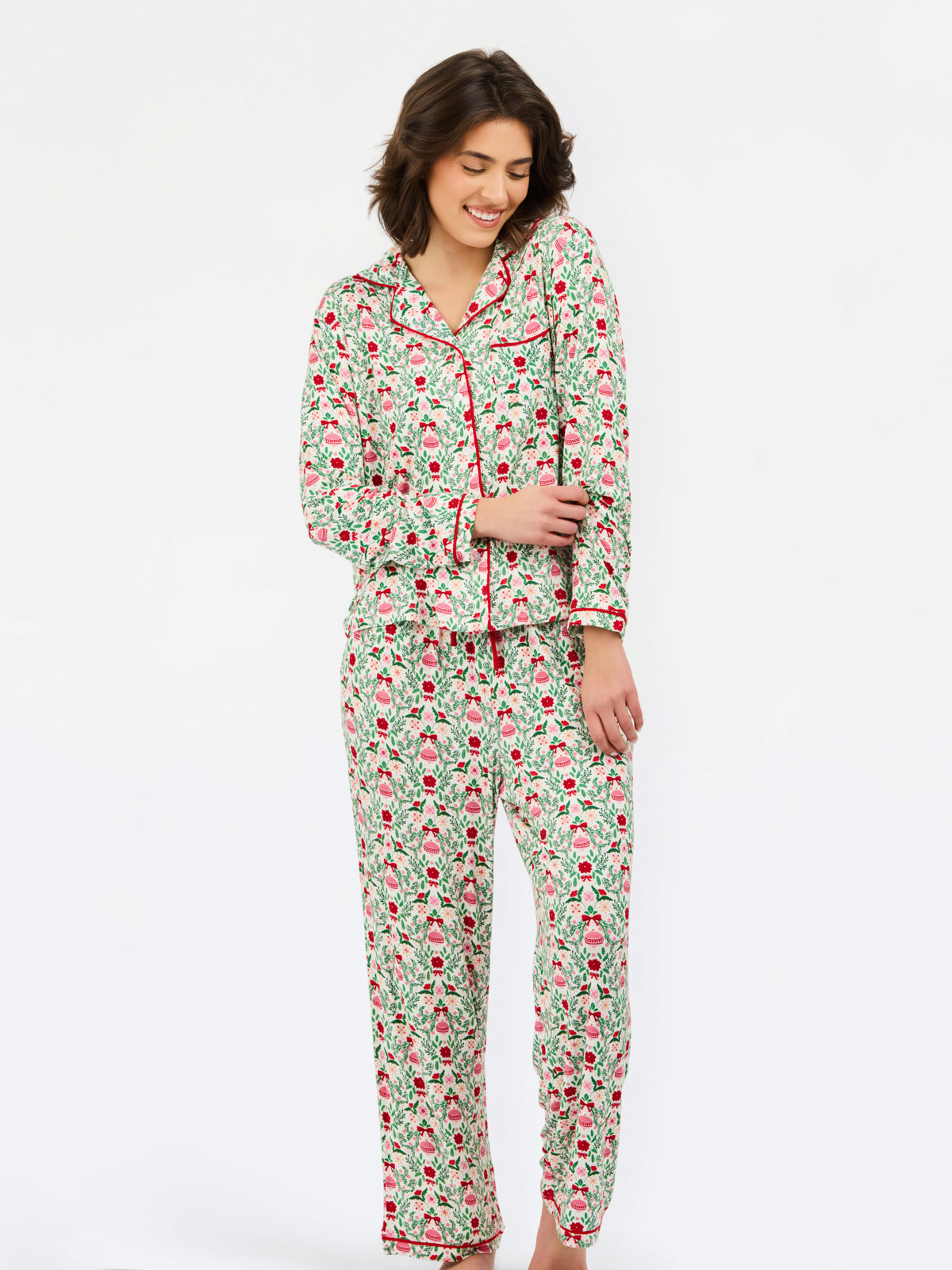 A woman modeling a two-piece pajama set with a green and pink floral print and red piping, standing against a plain white studio background.