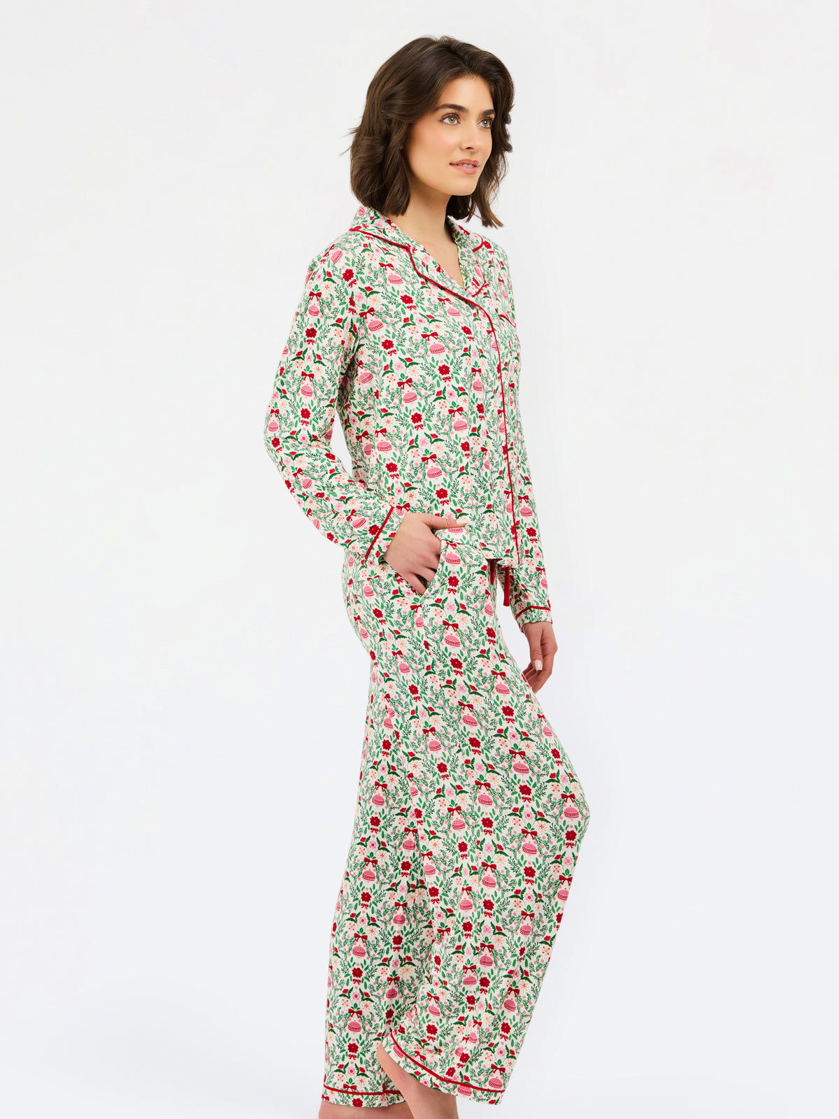 A woman modeling a two-piece pajama set featuring a long-sleeve button-up top and matching pants, both printed with a green, pink, and red strawberry pattern on a white background.