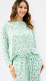 A woman modeling a matching two-piece lounge set featuring a light green and white watercolor-style pattern of houses and trees, with a long-sleeve top and drawstring waist.